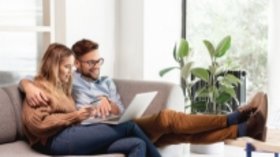 Mann und Frau auf Couch in Wohnzimmer mit Laptop auf dem Schoß