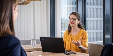 LIWEST Mitarbeiterinnen im Gespräch. Eine Person vor Laptop mit erklärenden Gestiken, die andere Person hört zu.
