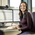 Mitarbeiterin vor zwei Bildschirmen. Sie lächelt in die Kamera und auf den Bildschirmen sind man Programmiercode.
