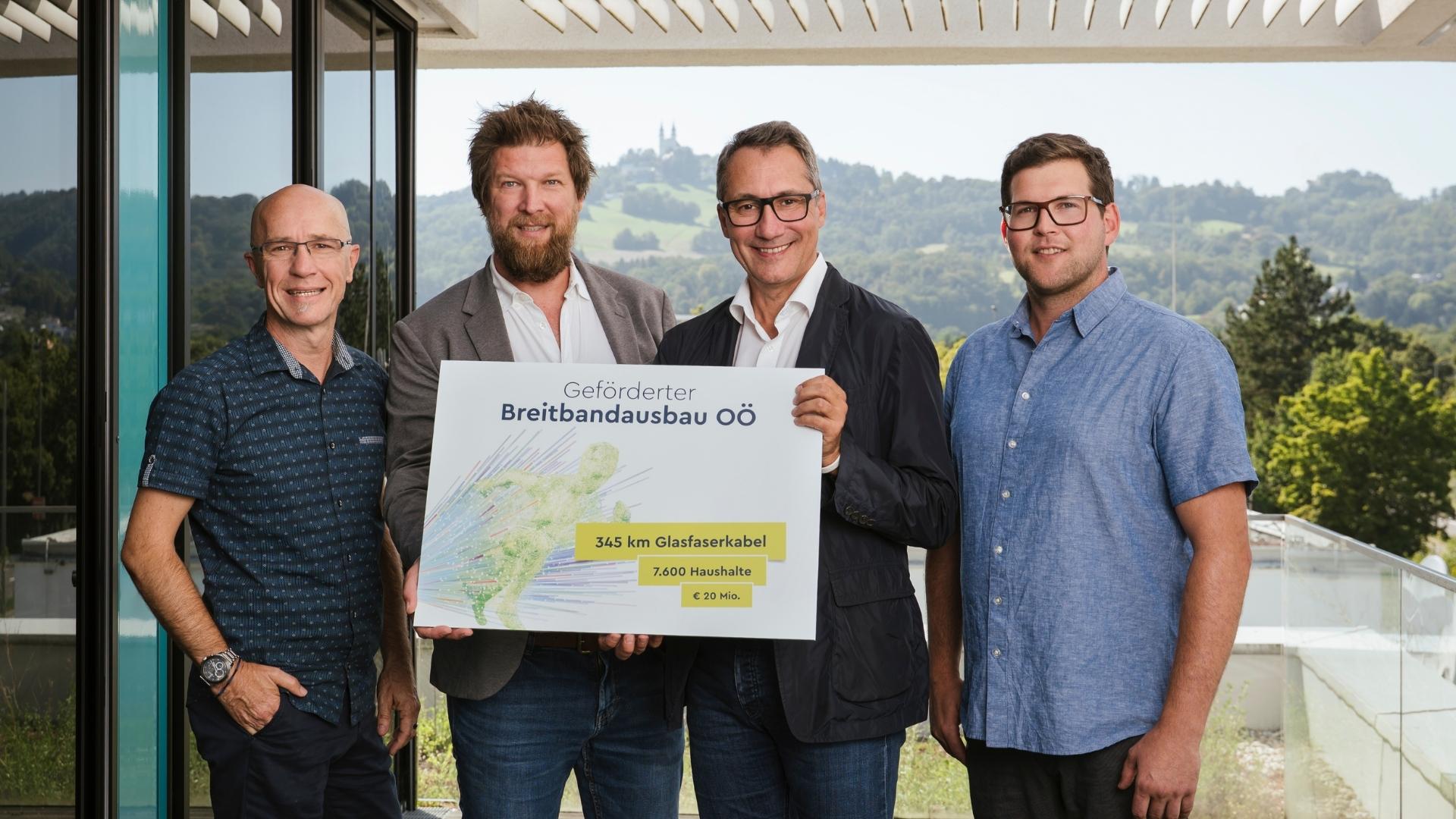 Gruppenfoto mit vier Personen auf Terrasse LIWEST Gebäude mit Blick Richtung Pöstlingberg, mittleren beiden Personen halten Schild mit Eckdaten zum geförderten Breitbandausbau OÖ