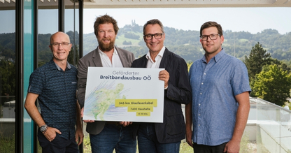 Gruppenfoto mit vier Personen auf Terrasse LIWEST Gebäude mit Blick Richtung Pöstlingberg, mittleren beiden Personen halten Schild mit Eckdaten zum geförderten Breitbandausbau OÖ