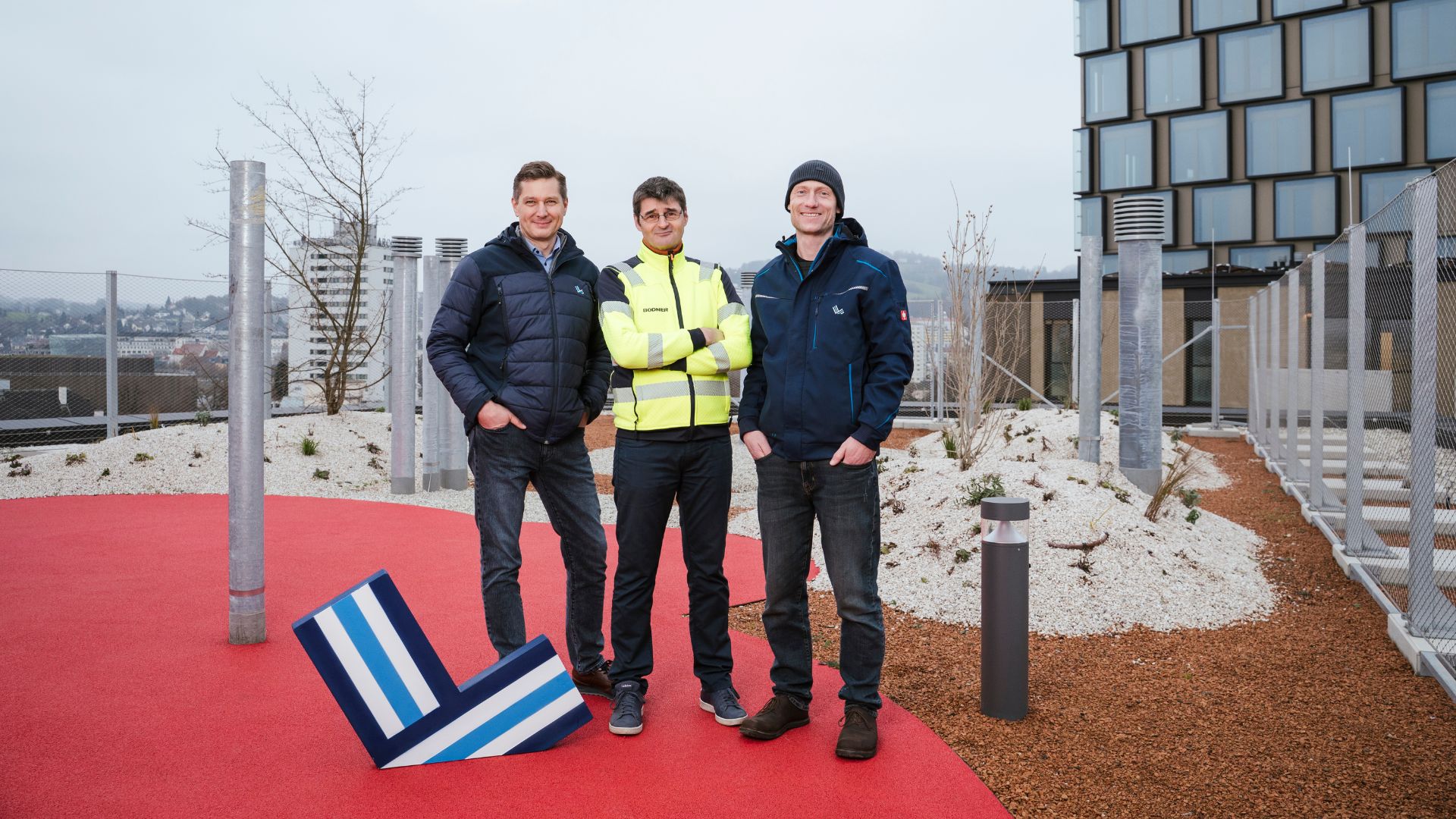 Reinhold Kaiser (LIWEST), Stefan Rützler (Bodner) und Alexander Mahringer (LIWEST) am Dach des Haus Boston mit dem Quadrill Tower, der Donau und die Stadt Linz im Hintergrund