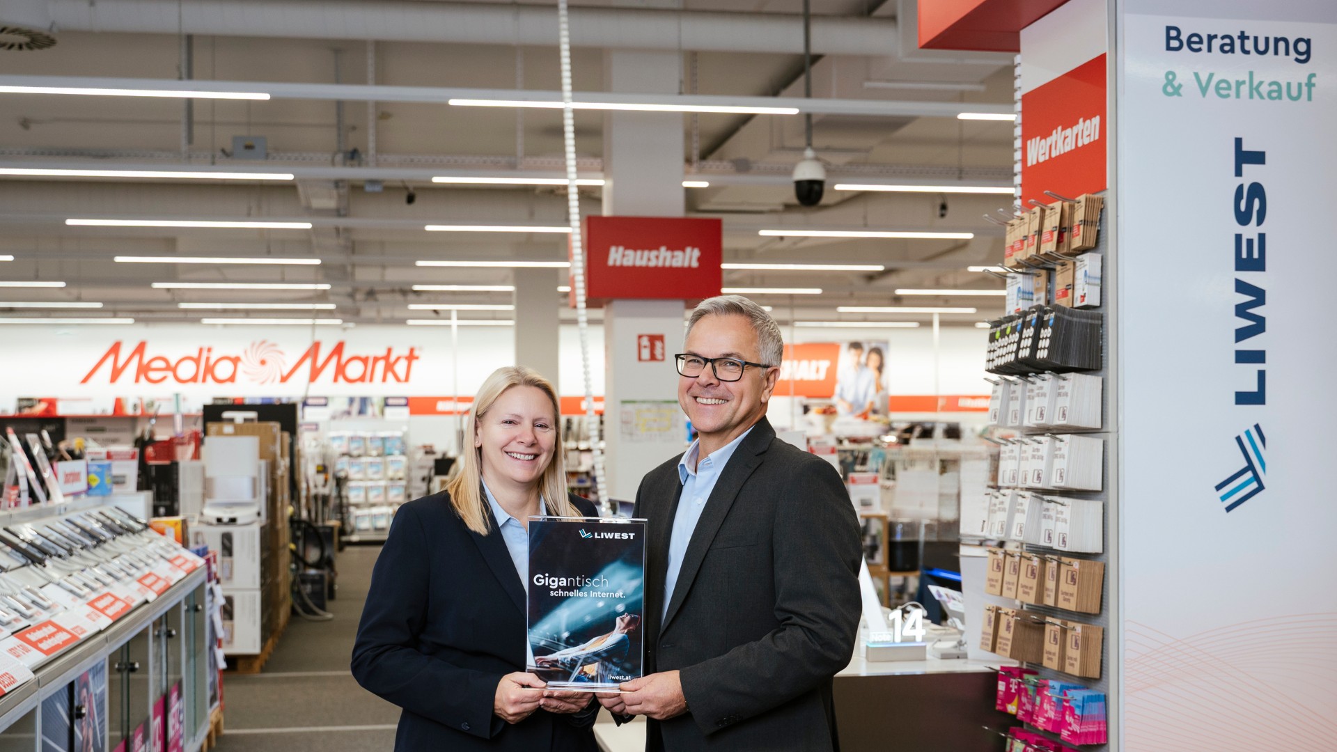 Daniela Zwieb (MediaMarkt) neben Robert Böhm (LIWEST) in Telekom-Abteilung im MediaMarkt Linz Industriezeile mit Schild Gigantisch starkes Internet von LIWEST in den Händen