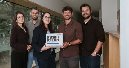 Zwei Damen, drei Herren in Schulgang, Dame und Herr in der Mitte halten die Medienkompetenz-Box