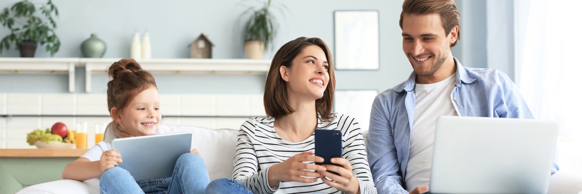 LIWEST Internet Super 2025 Familie mit Kind/Tabelt, Mutter/Mobiltelefon und Vater/Laptop auf Couch