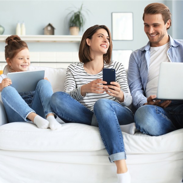 LIWEST Internet Super 2025 Familie mit Kind/Tabelt, Mutter/Mobiltelefon und Vater/Laptop auf Couch