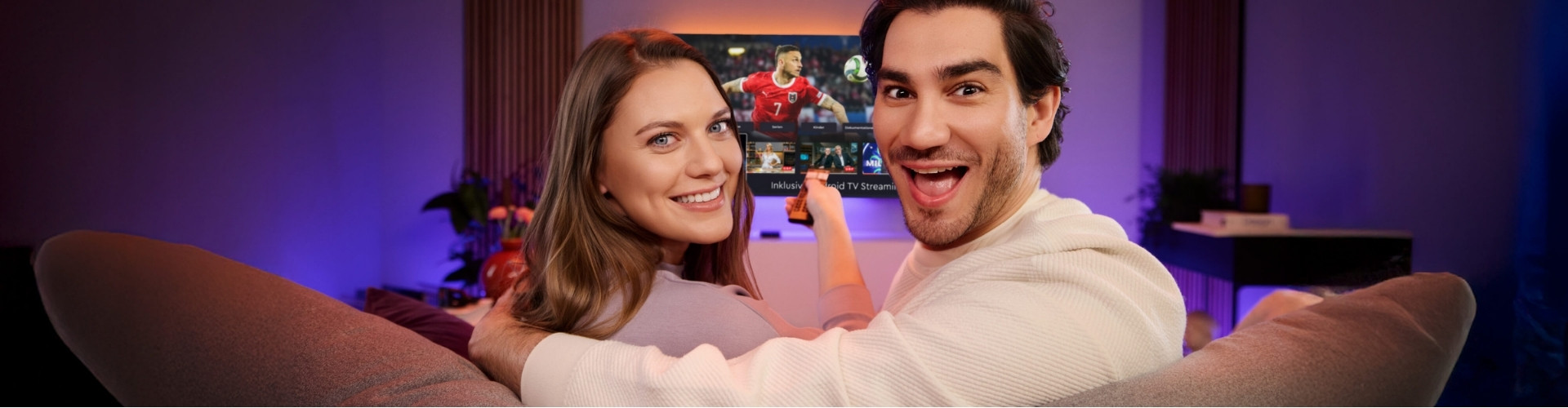 Päarchen auf Couch und Fernseher im Hintergrund