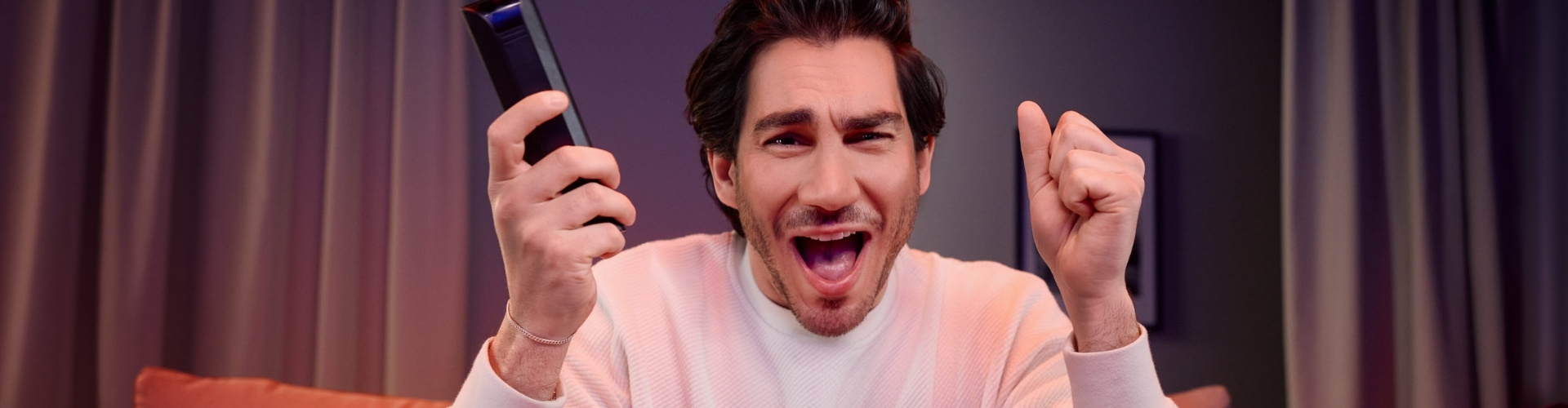 Mann mit Fernbedienung in der Hand jubelnd vorm Fernseher