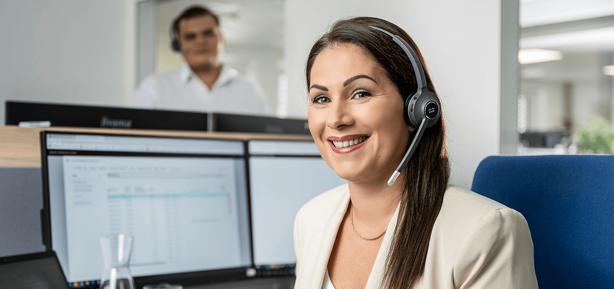 LIWEST Kundendienst Mitarbeiterin lächelnd vor Computerbildschirmen mit Headseat